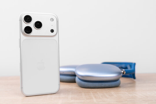 Bar, Montenegro: February 6, 2026: White apple iphone 17 pro standing beside blue airpods max headphones lying on light wooden table, premium audio technology concept