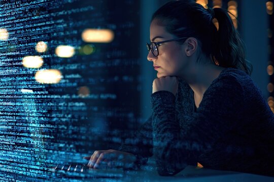 Programmer working late on computer coding software with digital data on screen