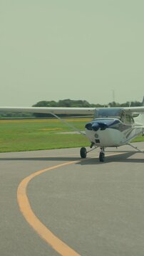 Small single engine Cessna 172 aircraft taxis along curved taxiway line then comes to complete stop near airport hangars