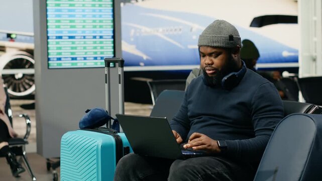 An African American worker uses a laptop in relaxed clothing while waiting at the airport for an international business flight abroad.