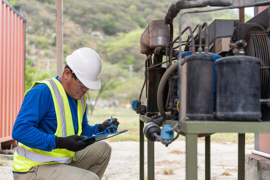 Technician inspecting industrial engine outdoor with clipboard