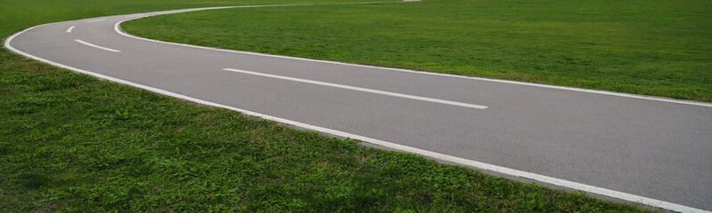 Obraz premium empty Winding curvy path through a lush green grass park Winding Pathway Gray black asphalt road Green Grass central park Woods Nobody
