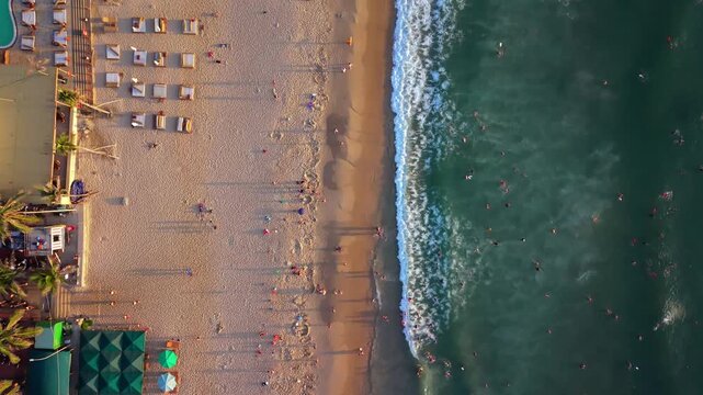 Vertical aerial drone footage looking straight down over My Khe Beach, capturing emerald sea, gentle waves and beachgoers enjoying the coastline in Da Nang, Vietnam.