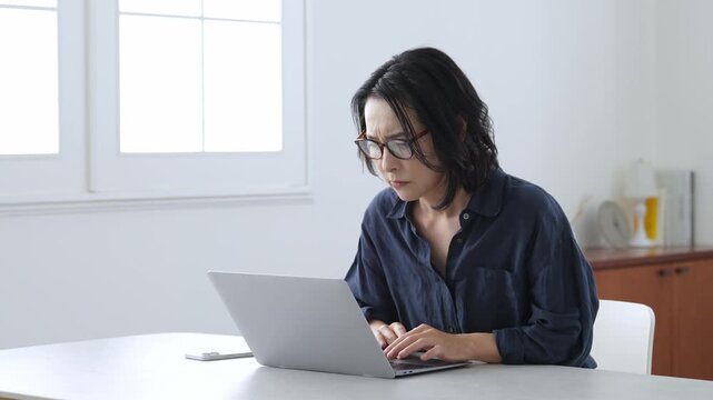 困った表情でパソコンとスマートフォンを使う中高年女性