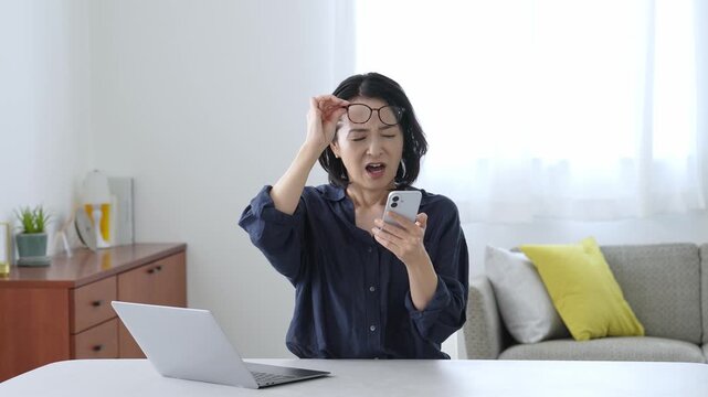 困った表情でパソコンとスマートフォンを使う中高年女性
