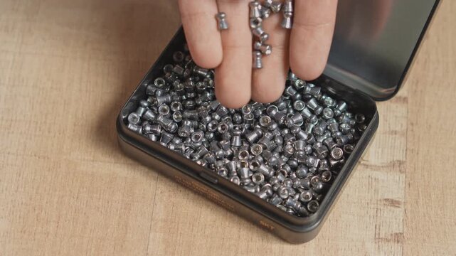 Hand taking airgun pellets out of metal tin box filled with ammunition on wooden table video slow motion concept
