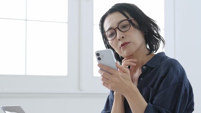 困った表情でスマートフォンを使う中高年女性