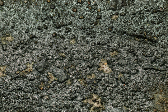 Extreme close up texture of wet rough dark concrete stone surface with sparkling moisture details