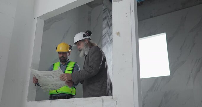 Engineer and businessman reviewing blueprint construction plans at house building site
