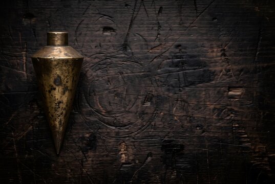 Vintage heavy solid brass plumb bob on dark wooden workbench with copy space