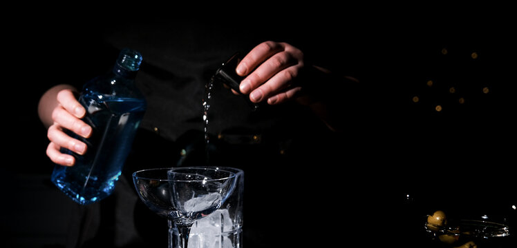 Nightclub bartender pouring clear spirit from blue bottle into steel jigger. Precise alcohol measurement concept.