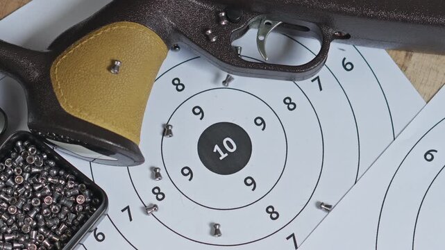 Small metallic pellets fall across paper shooting targets alongside air rifle and tin box of ammunition video slow motion concept