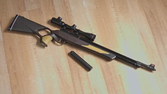 Full layout of sniper airgun with optical scope and silencer on wooden table