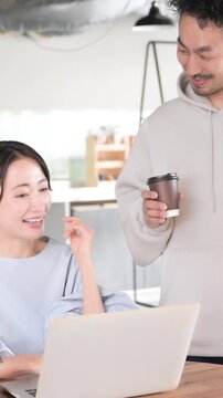 仲良く会話する日本人の男女ビジネスパーソン、笑顔の同僚、職場のコミュニケーション、休憩や雑談を楽しむ縦動画　オフィス回帰イメージ