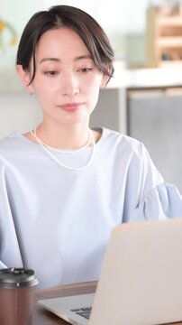 オシャレな明るいオフィスでノートパソコンで仕事をする日本人女性 オフィスワーク・ビジネスシーン　コーヒーを飲む縦動画