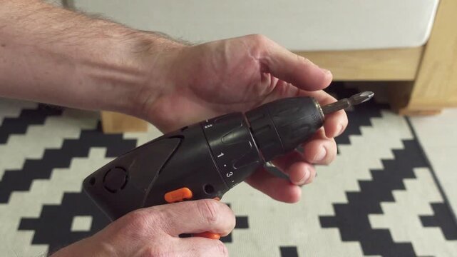 Close up of a man holding the chuck and pressing the trigger to release the bit, turning the bit around and holding the chuck again to tighten the bit. 


