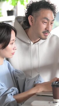 パソコンを仕事で一緒に画面をのぞき込む男女のオフィスワークのビジネスシーン、相談や打ち合わせイメージ縦動画