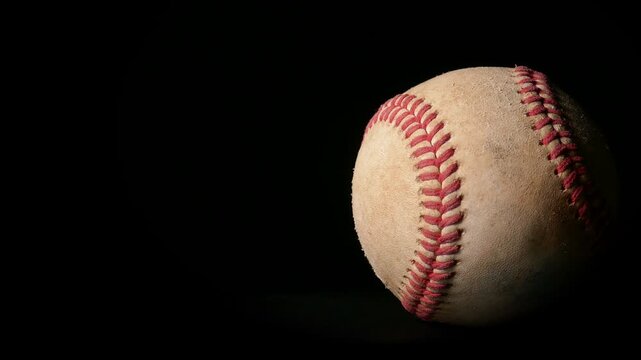 A well worn baseball rotating isolated against a black background. Sports or game ball concept with copy space.