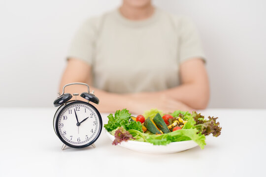 happy smiling woman with fresh organic vegetables plate and alarm clock. intermittent fasting, IF, meal time, nutrition, weight loss, clean eating, Healthy food eating, Wellness, dieting and lifestyle