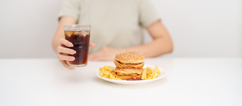 woman eating Juicy beef burger with melted cheddar cheese, potato chips and carbonated Soft drinks. Unhealthy, High calorie, Fast food craving, Obesity, diet, weight loss, junk food and lifestyle