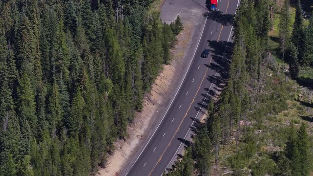 Aerial of Highway 97 through Okanogan Wenatchee National Forest Washington with dense evergreen forest on both sides and several vehicles traveling along the winding path
