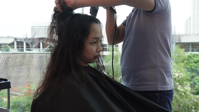 Hair stylist blow drying long hair before hair coloring treatment in salon for Southeast Asian woman in her early 20s