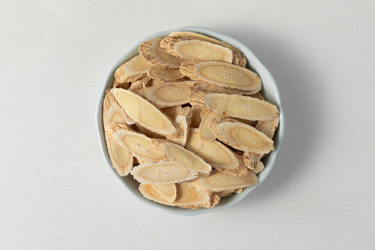 Top view of dried Astragalus root slices in a ceramic bowl on light background, traditional Chinese herbal medicine