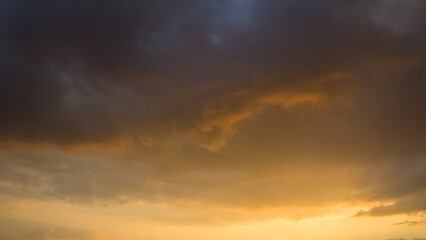 Fototapeta premium Dramatic golden sunset sky with dark storm clouds. Beautiful natural background of evening sun filtering through heavy clouds before rain.