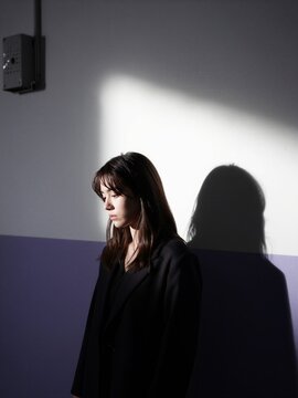 Moody portrait of a contemplative woman in a black blazer against a shadowed wall