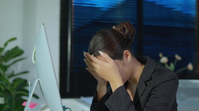 Overworked Asian businesswoman feeling tired and stressed while working late at night in the office, showing signs of burnout, fatigue, headache, and pressure from an intense workload