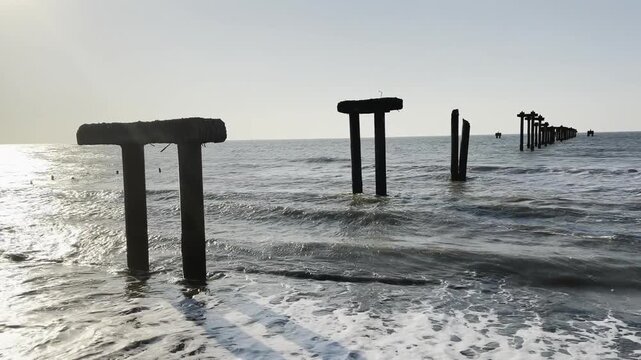 Remnants of a forgotten wooden pier standing resiliently in the gentle sea waves along the coast