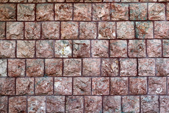 Reddish stone wall texture with square chiselled blocks and rough surface