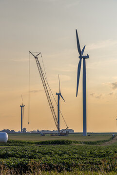 Full frame landscape view of giant wind-powered electrical generators in an agricultural field on a sunny day, with cview of a crane.
