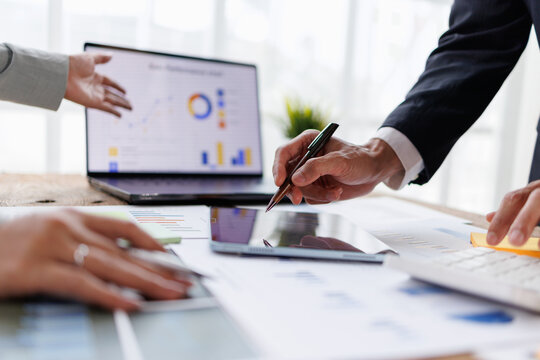 Business professionals analyzing financial data and charts on a laptop and tablet, collaborating on corporate strategy and investment planning during a modern office meeting