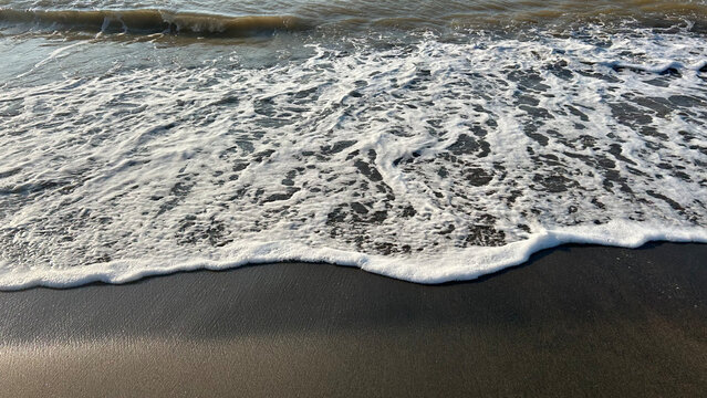Sea waves with white foam washing onto the dark sandy beach shore