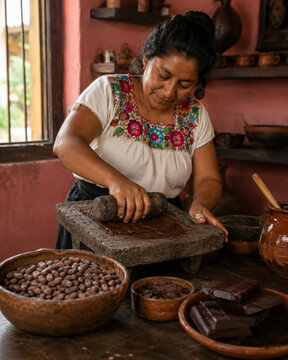 Indigenous woman manually grinding roasted cacao beans on a traditional stone metate