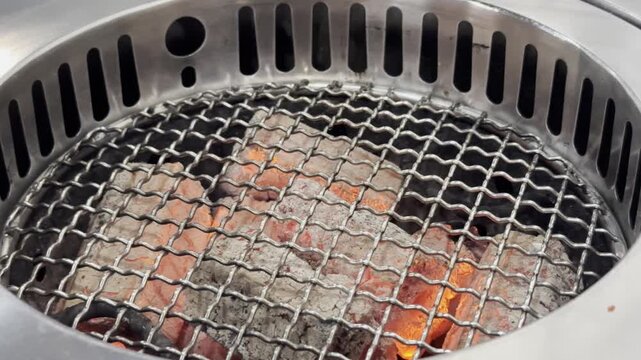 Close-up of an empty barbecue grill with glowing charcoal embers, rising heat, and smoky atmosphere, ready for outdoor grilling and cooking.