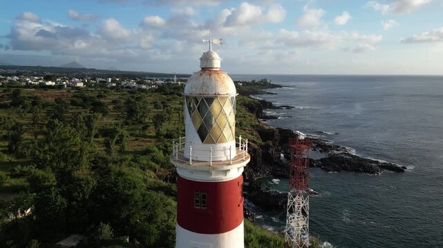 Close-up drone lantern room of Albion Lighthouse in Mauritius. Aerial view of the historic beacon with rocky coastline, ocean and coastal village in the background
