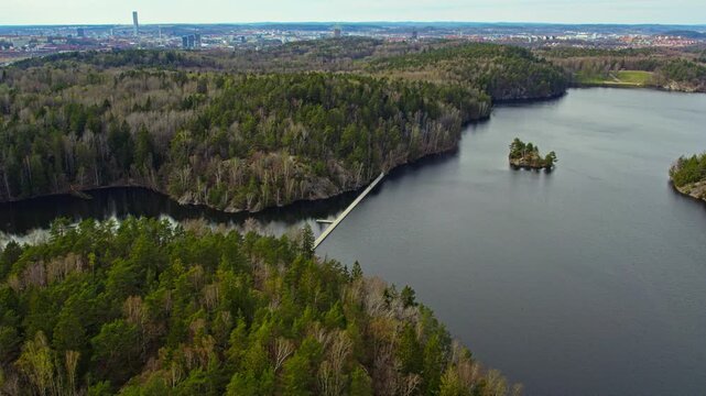 Drone view of a wooden floating bridge across Stora Delsj&ouml;n lake in Gothenburg, Sweden. The footage shows the bridge nestled in a lush green forest landscape within a popular nature reserve.