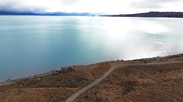 Forward aerial drone footage flying from the shoreline out over Lake Pukaki, revealing turquoise glacial waters, rugged terrain, and stunning alpine scenery in New Zealand.