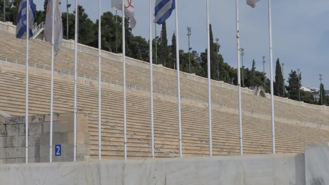 Marble seats of the ancient Panathenaic Stadium, Kallimarmaro, with waving Greek and Olympic flags. Panning Shot