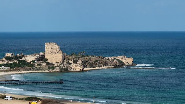 High angle static shot focusing on the stone ruins of Chateau Pelerin fortress situated on a promontory overlooking turquoise sea water under a clear blue sky