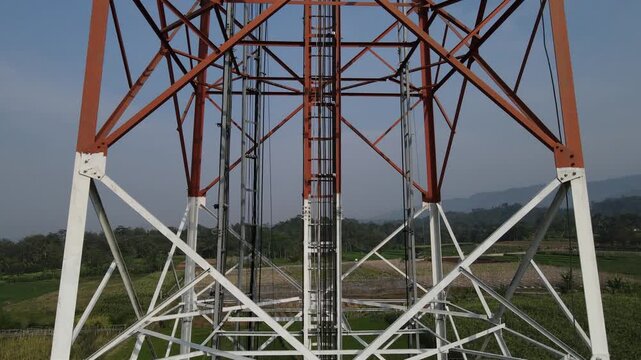 Close-up aerial video of the radio masts and steel structure on a telecommunications tower against a clear morning sky, Captured from above.