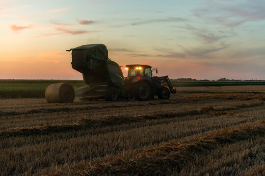 Round hay bale being ejected from baler during evening harvest