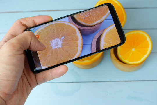 A person using a smartphone to take a photo of fresh sliced oranges in wooden bowls, representing food photography, concept content creation, and mobile technology. 