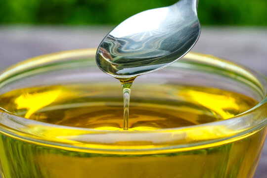 The image of golden oil dripping from a spoon into a glass bowl symbolizes healthy cooking, organic ingredients, nutritional value, and well-being in cooking &ndash; the concept of healthy eating.