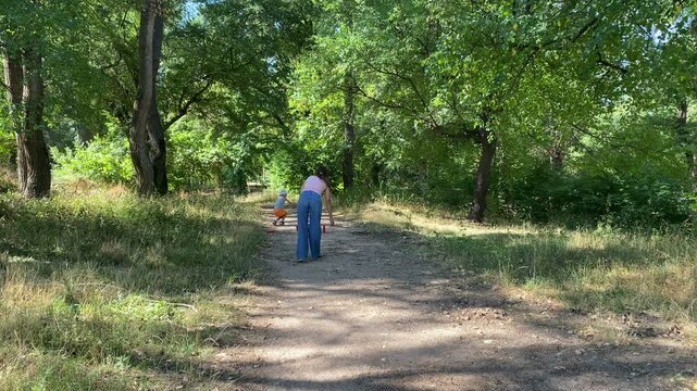 A relaxed woman walks peacefully down a dirt path. She moves gently toward toy hurdles in the distance. Tall green trees shade the calm, beautiful forest.