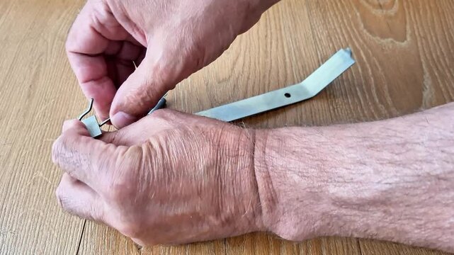 A person installs a tension spring onto a metal hook using hand tools, demonstrating a precise fastening process. Suitable for DIY, mechanical repair, maintenance, engineering