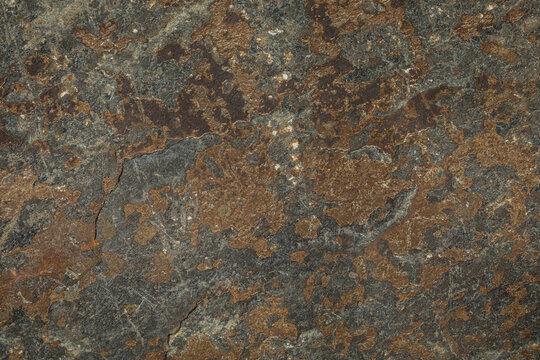 Natural rusty ironstone slate stone texture with rough mineral surface background. Weathered iron mineral deposits, dark grey slate layers, and subtle cracks.