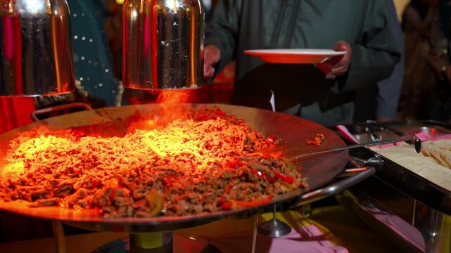 Freshly cooked stir fried noodles with beef and vegetables on a large catering flat-top grill.